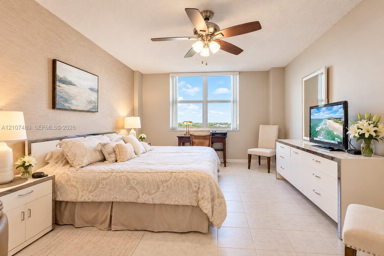 Neutral-toned interior space featuring large windows, textured wall surfacing, neutral tile flooring, and a multi-blade ceiling fan with integrated lighting