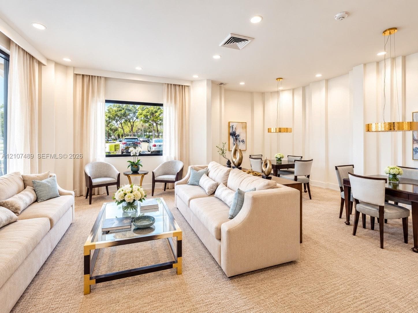Expansive living space featuring neutral-toned carpeting, recessed ceiling lighting, textured wall detailing, and dual circular gold-tone pendant fixtures