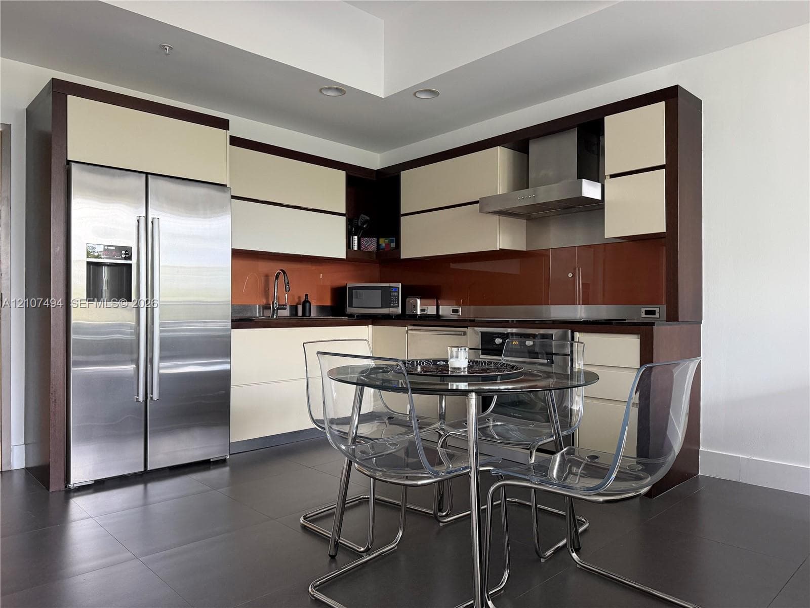 Modern kitchen featuring two-toned cabinetry, stainless steel appliances, a glass-panel backsplash, and dark tile flooring