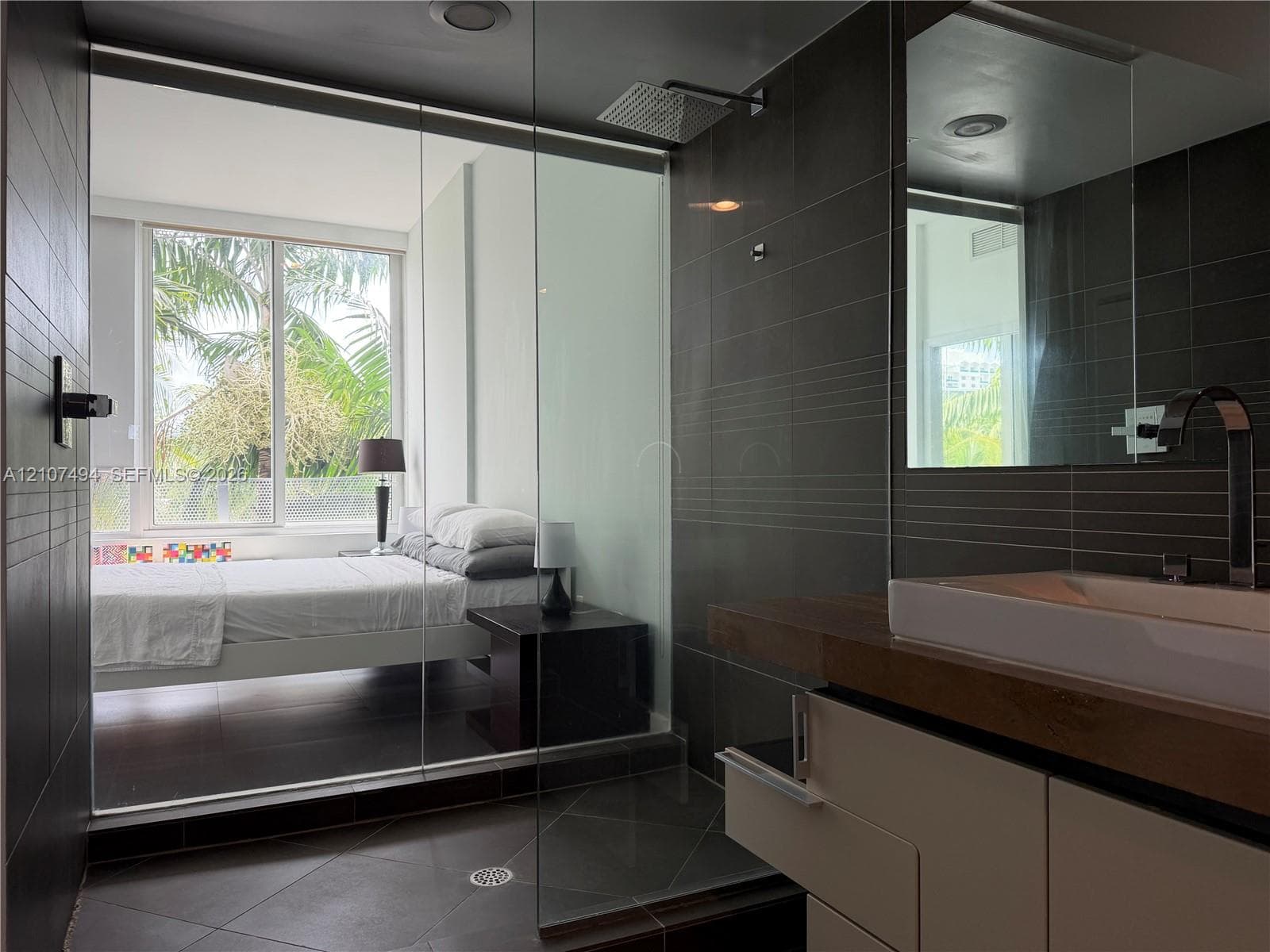 Bathroom featuring large-format dark wall and floor tile, glass-enclosed shower with a rainfall showerhead, and a floating vanity with a vessel sink and contemporary faucet