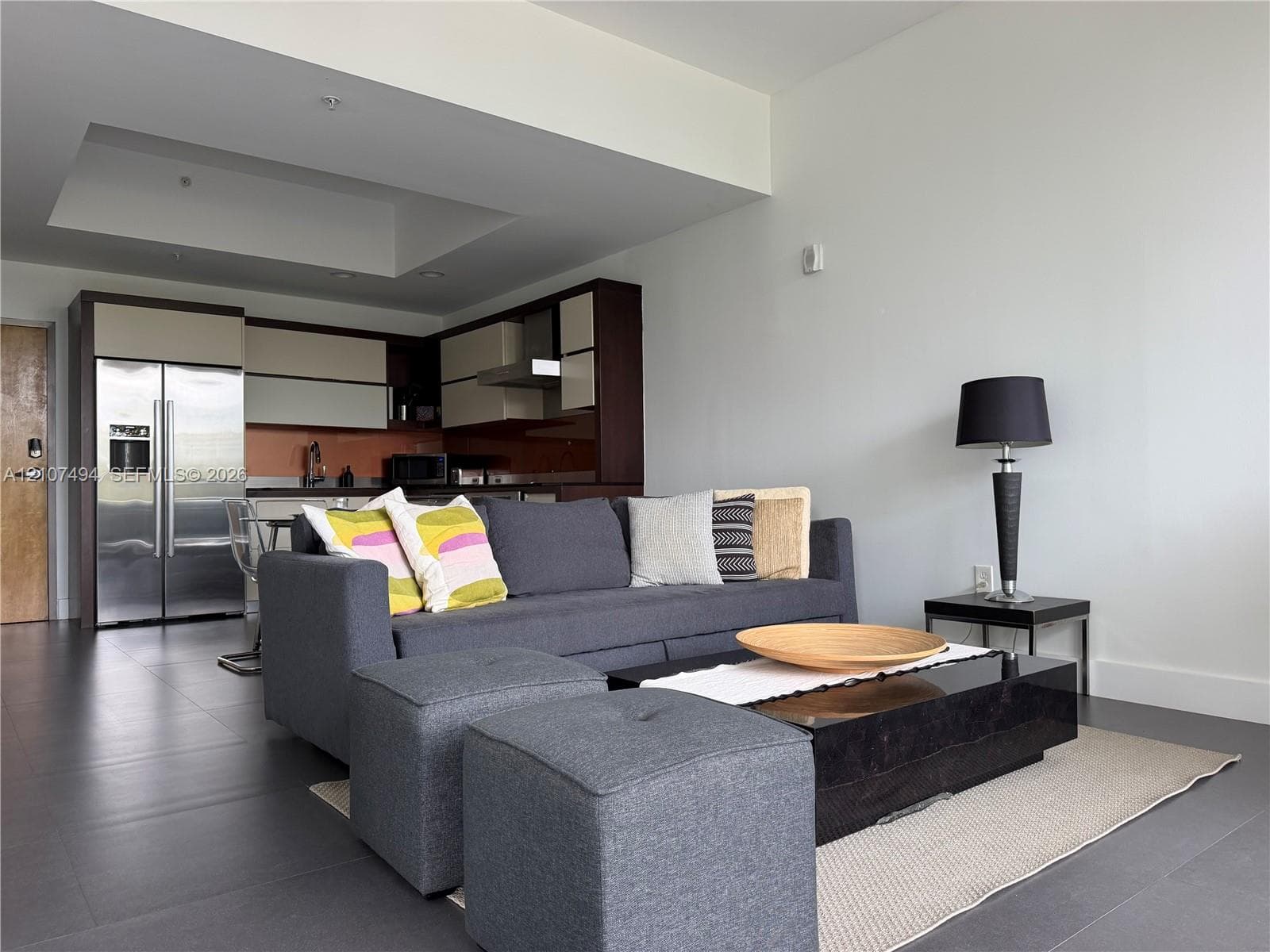 Open-concept area featuring oversized neutral floor tiling, recessed ceiling detail, and kitchen cabinetry with a two-tone finish