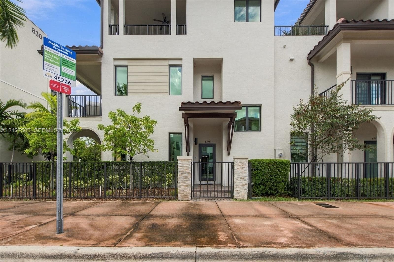 Stucco exterior featuring multi-level balconies, stone-accented entryway, tile roofing, and metal perimeter fencing