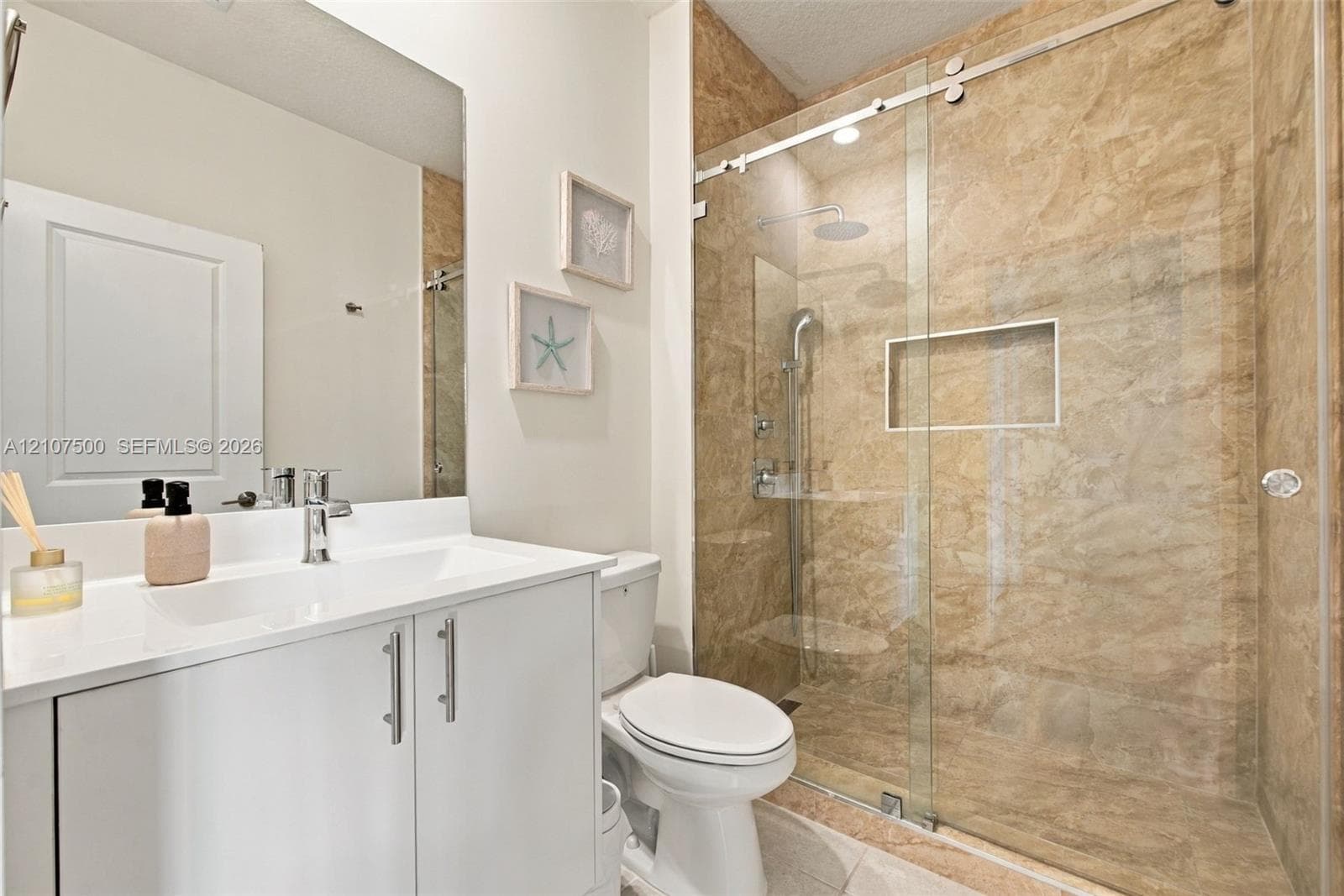 Bathroom featuring a white vanity with a rectangular sink, a frameless glass shower enclosure with sliding hardware, stone-finish wall tile, and a recessed shower niche