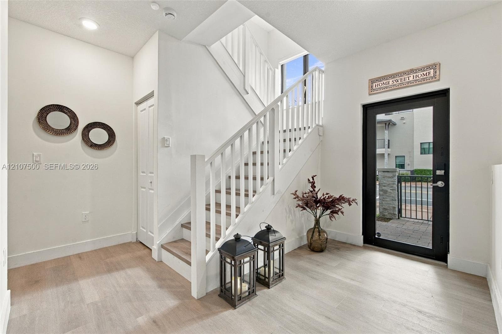 Foyer featuring wood-finish flooring, a glass-panel entry door, and a staircase with white painted balusters and wood-finish treads