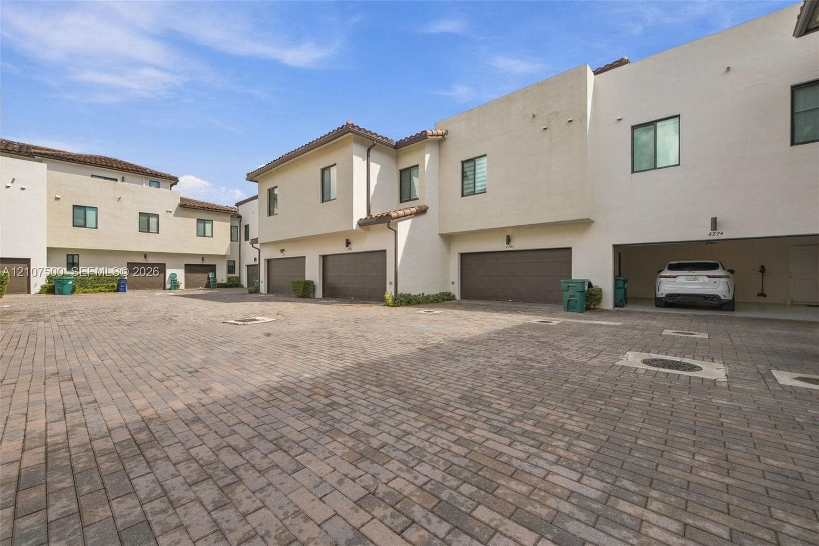Multi-unit exterior featuring stucco siding, tile roof accents, paved brick driveway, and integrated garage parking