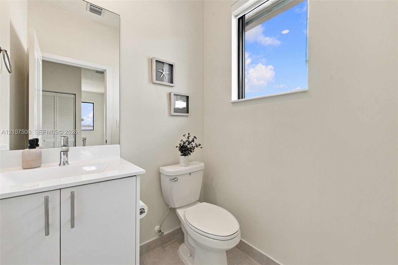 White vanity featuring a rectangular integrated sink, chrome faucet, and vertical pulls, paired with an expansive wall-mounted mirror and a window