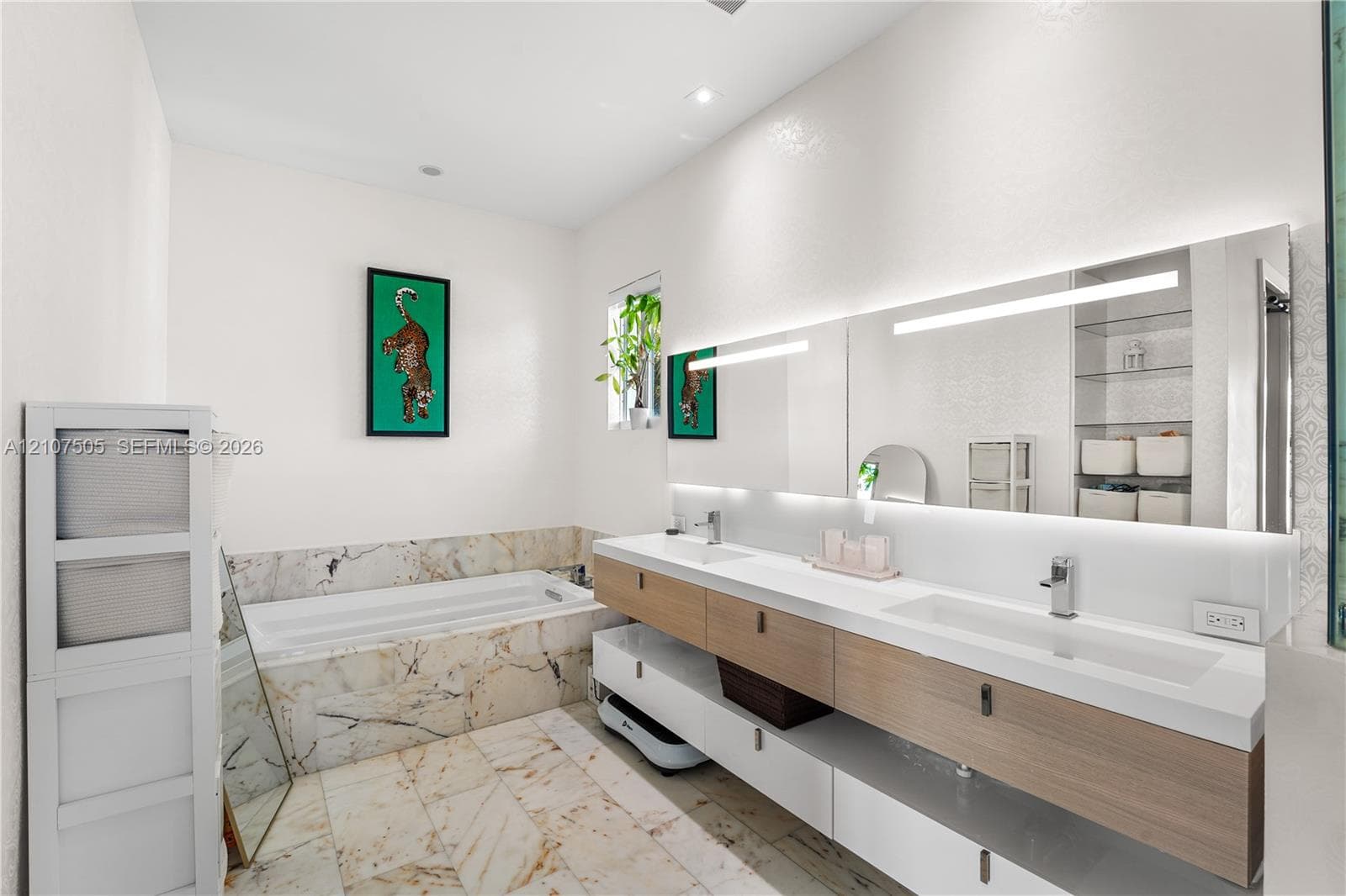 Floating dual vanity featuring wood-finish cabinetry, integrated sinks, and polished chrome faucets, complemented by a stone-tiled soaking tub and coordinating stone flooring