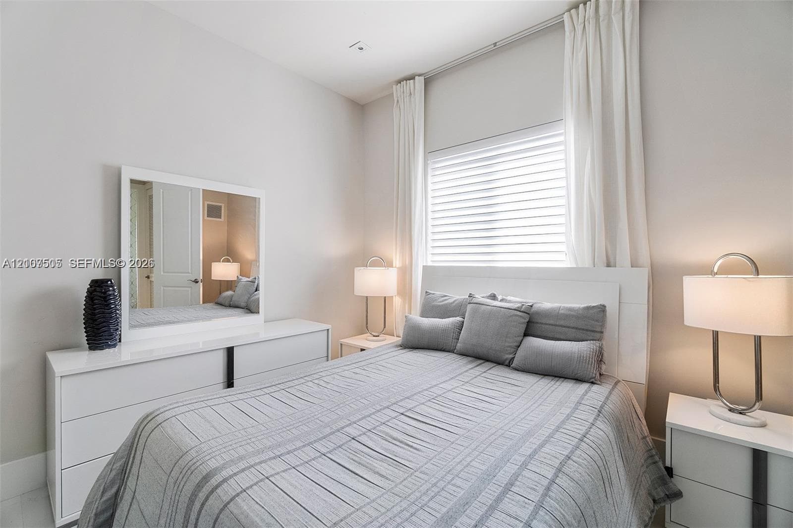 Bedroom interior featuring neutral wall paint, white trim, horizontal blinds, and ceiling-mounted curtain tracks