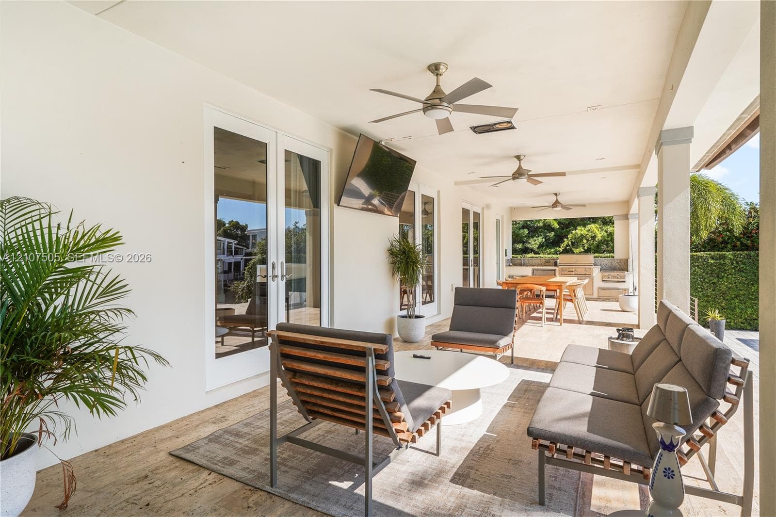 Covered outdoor living area featuring stone-finish flooring, ceiling fans, recessed lighting, and a built-in outdoor kitchen with stone masonry