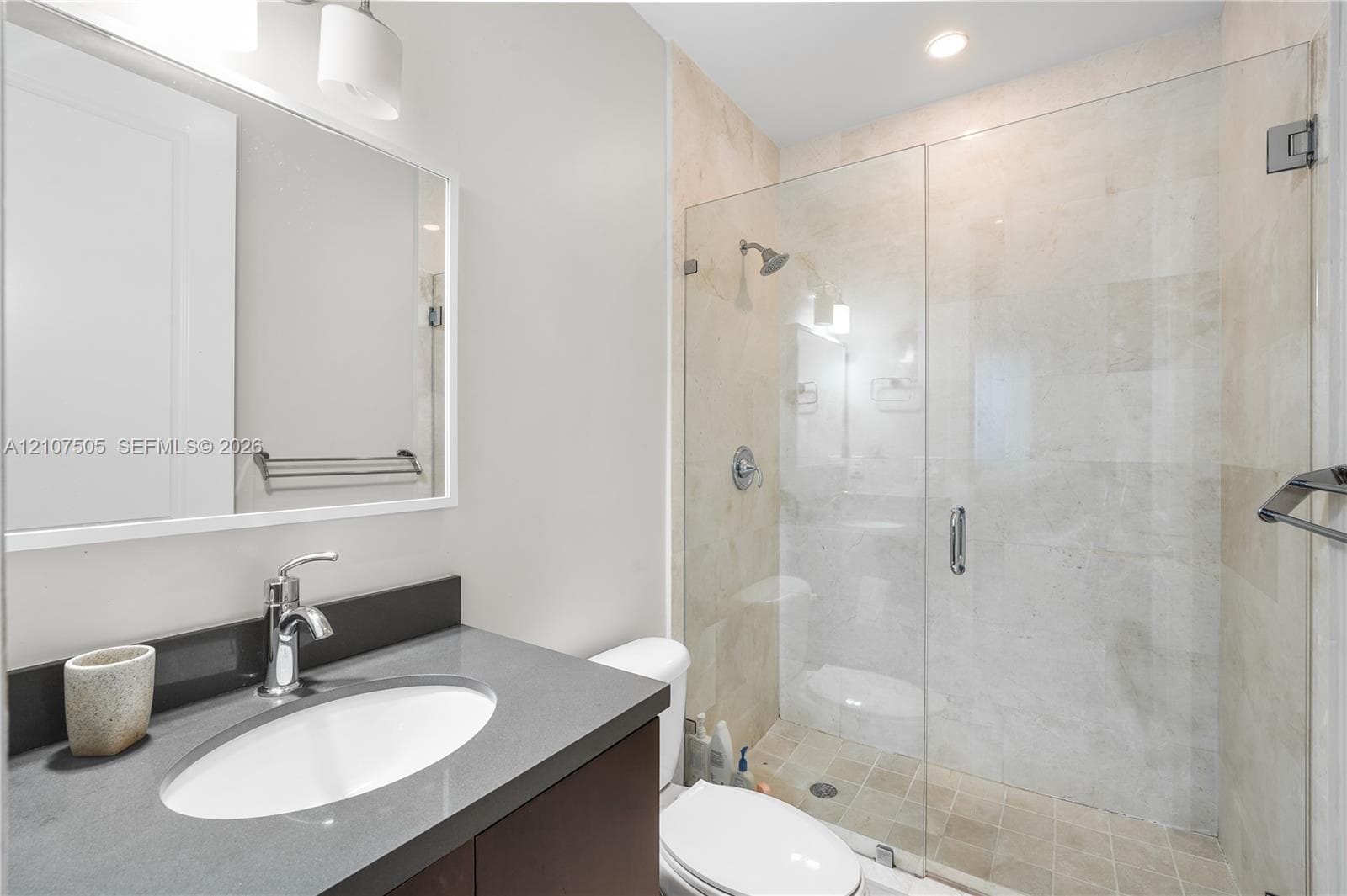 Bathroom featuring a stone-topped vanity with an undermount sink, a glass-enclosed shower with tile surround, and wall-mounted hardware