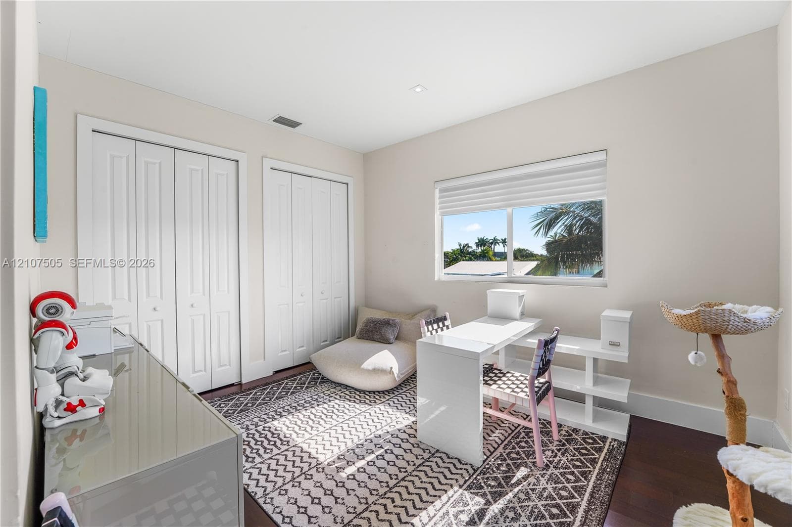 Neutral-toned room featuring dark wood-finish flooring, dual bi-fold door closets, recessed lighting, and a single-pane window with a roller shade