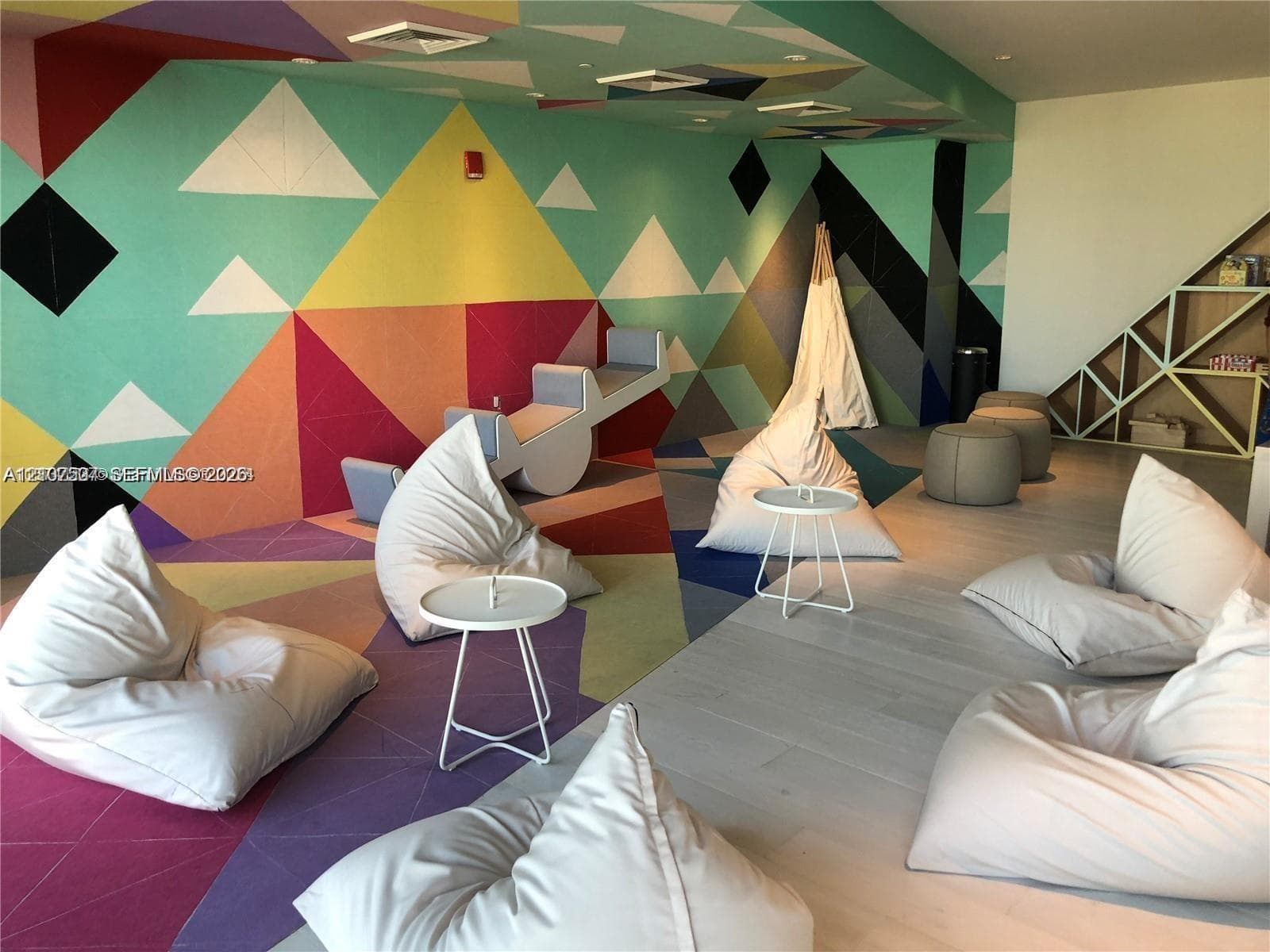 Geometric wall mural featuring multi-colored triangles, light-toned wood-finish flooring, and built-in angular shelving units