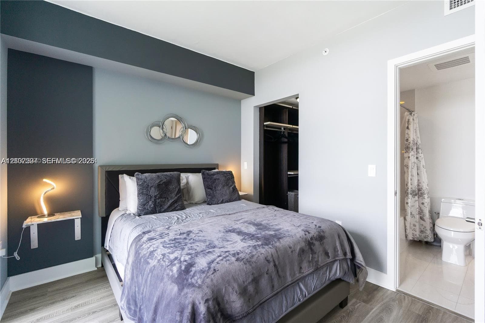 Bedroom featuring a dark-toned accent wall, wood-finish flooring, a floating stone-surface shelf, and a walk-in closet