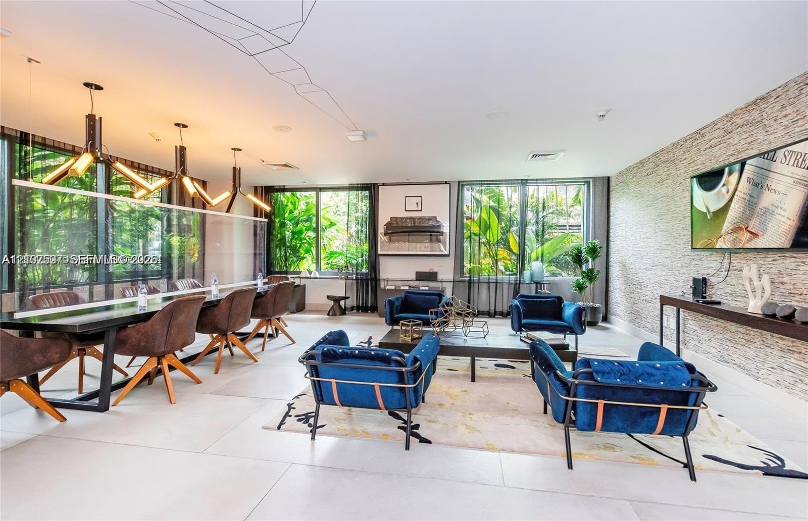 Open-concept living space featuring large-format tile flooring, a floor-to-ceiling textured stone accent wall, geometric overhead lighting fixtures, and expansive windows with greenery