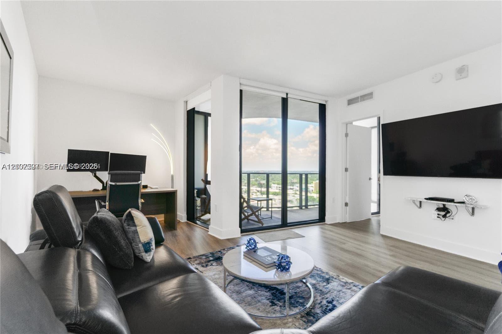 Living area featuring wood-finish flooring, floor-to-ceiling glass sliding doors, and a private balcony
