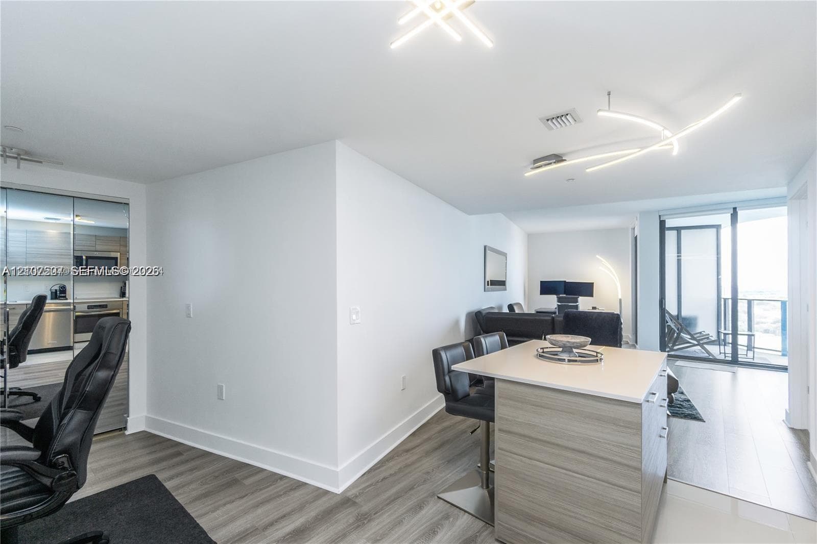 Open-concept living space featuring wood-finish flooring, a kitchen island with stone-composite countertop, and contemporary geometric ceiling-mounted LED lighting