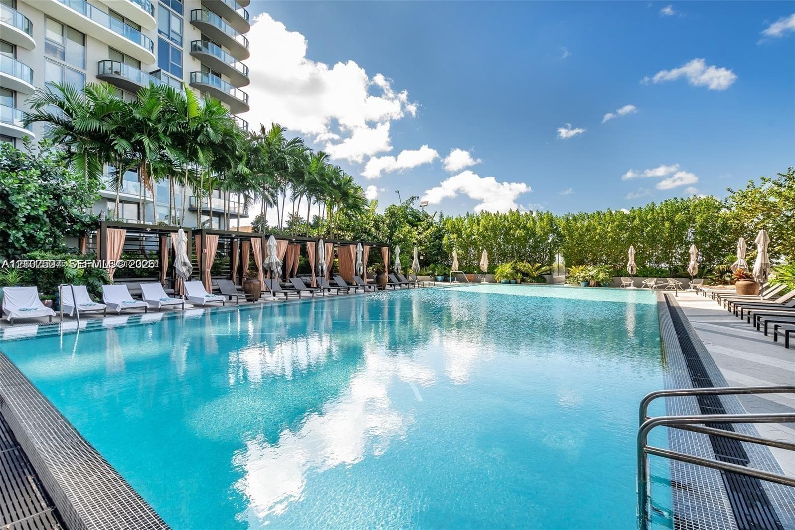 Outdoor swimming pool with a tiered tile perimeter, wood-frame cabana structures, and paved pool deck