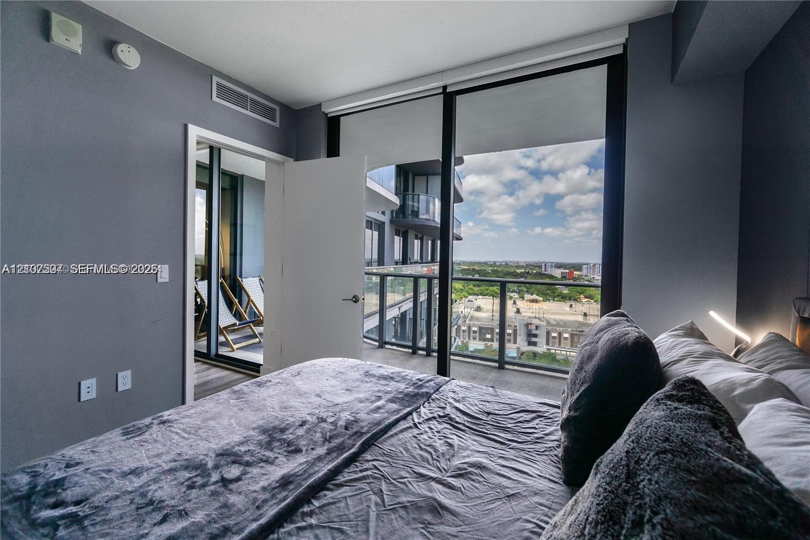 Floor-to-ceiling windows, private balcony with metal railing, and high-rise cityscape horizon