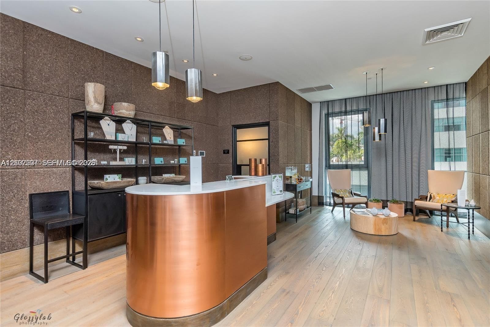Curved reception desk featuring a metallic finish and solid surface countertop, complemented by textured panel wall cladding, recessed lighting, and wood-finish flooring