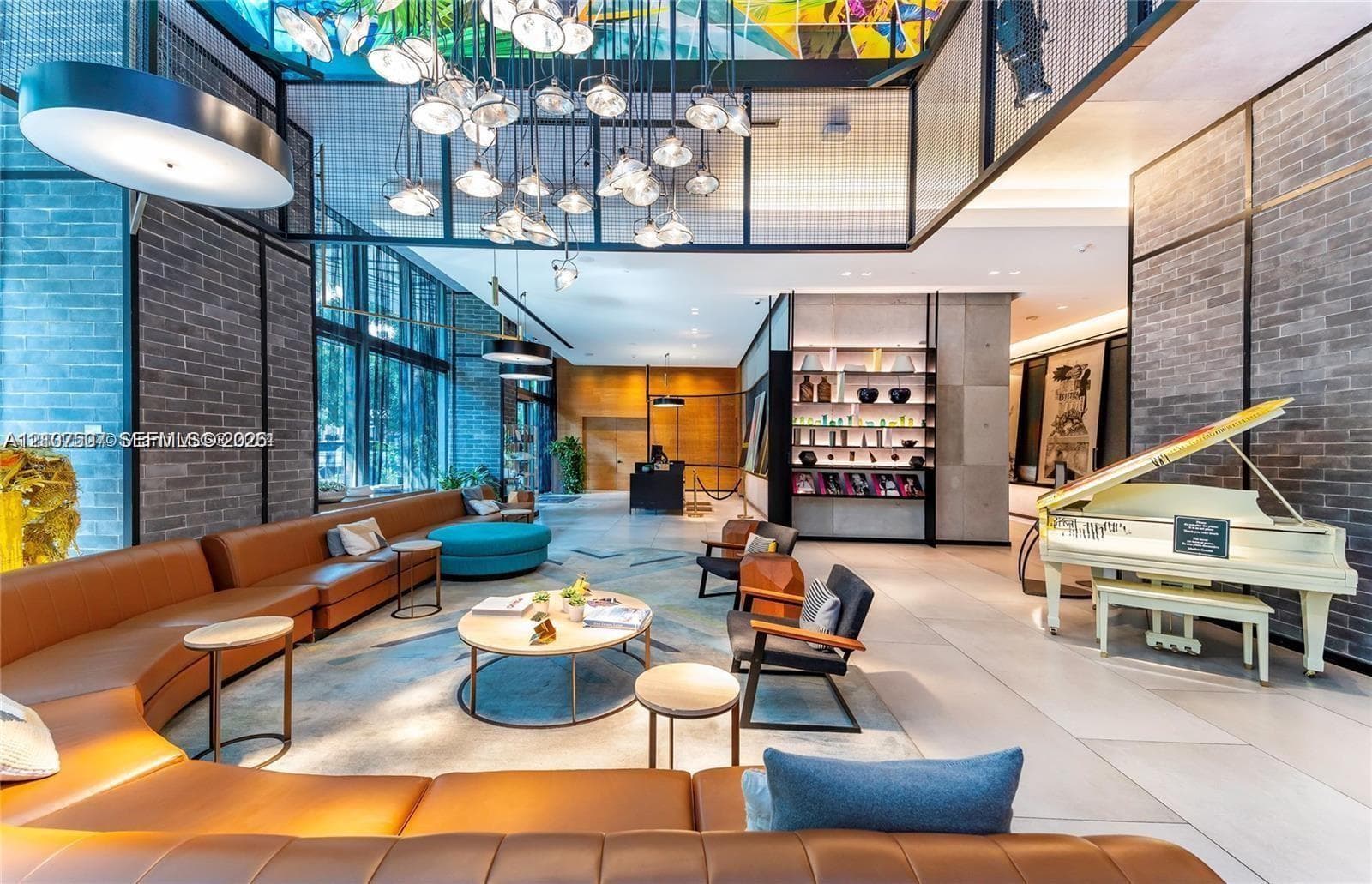 Expansive lobby area featuring floor-to-ceiling windows, exposed brick walls, stone flooring, a multi-tiered pendant light fixture, and recessed built-in shelving