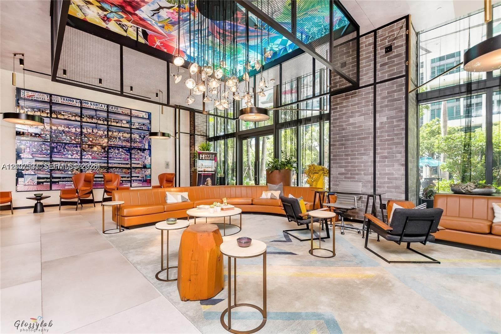 Expansive common area featuring floor-to-ceiling windows, brick accent walls, a multi-colored ceiling mural, and a contemporary multi-bulb chandelier