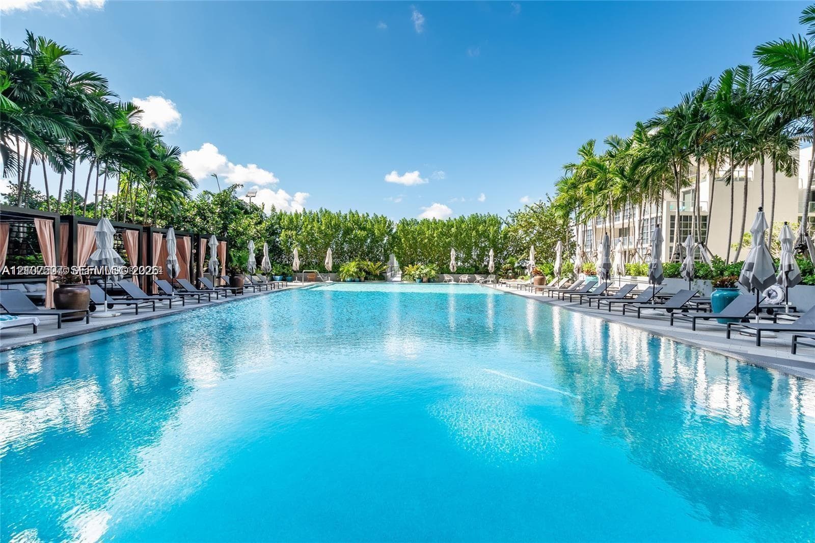 Expansive swimming pool featuring built-in cabanas, stone-tiled decking, and mature palm tree landscaping