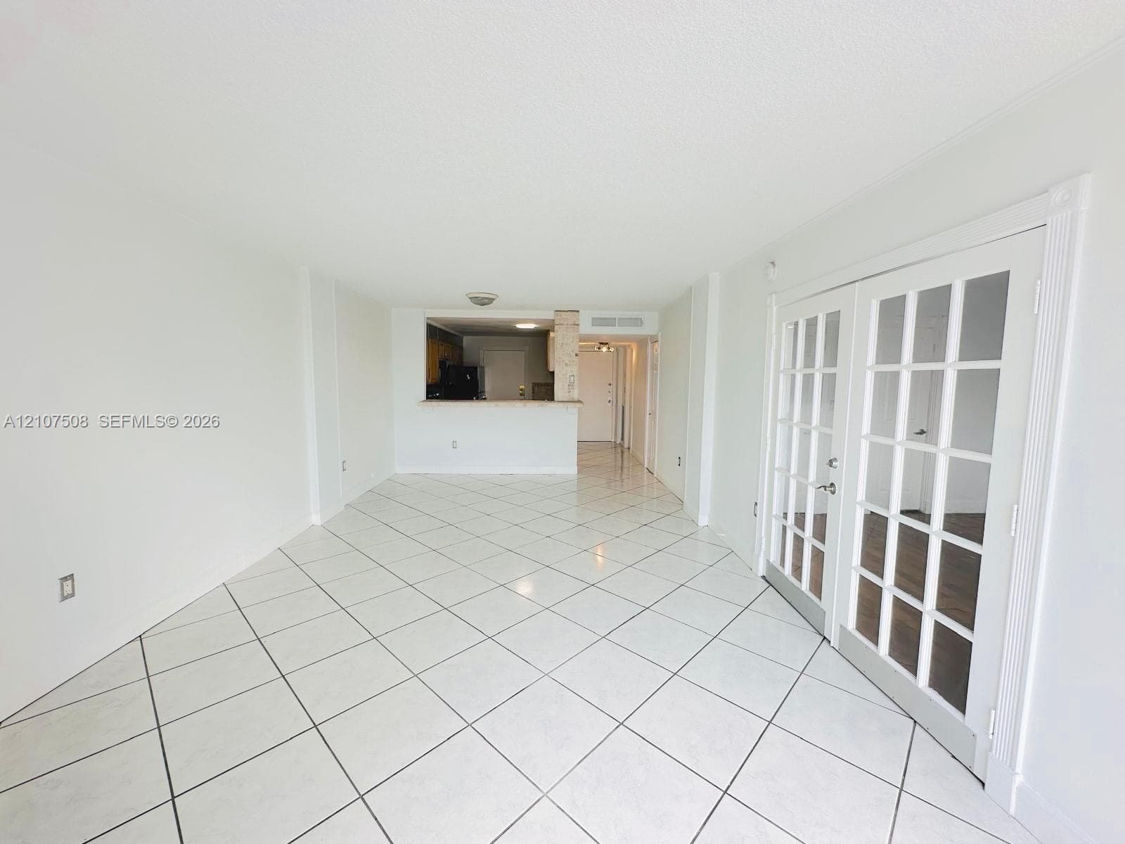 Large-format white tile flooring, French doors with glass panes, and a pass-through kitchen opening