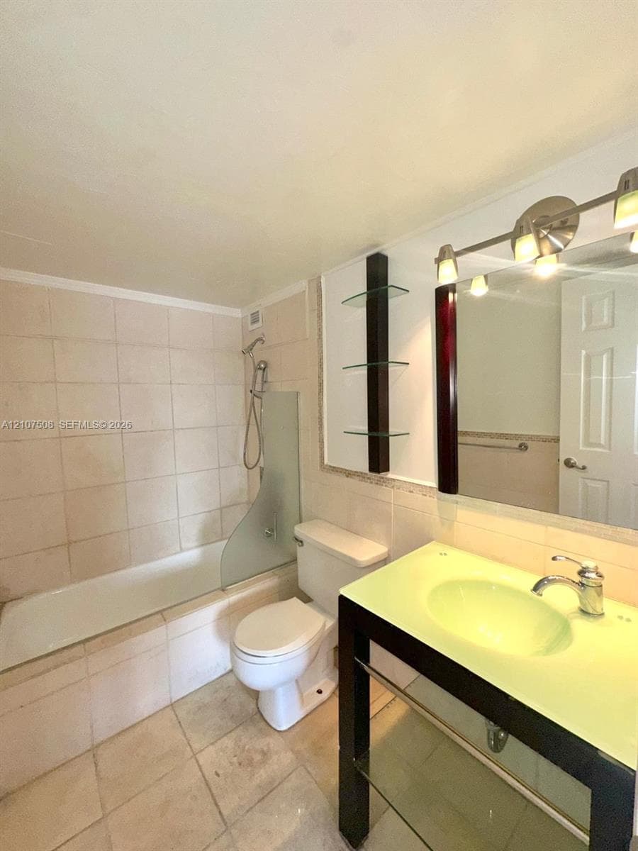 Bathroom featuring a pedestal vanity with a glass countertop, integrated sink, and tiered glass shelving, complemented by a tiled shower surround with a fixed glass splash panel and multi-light vanity fixture