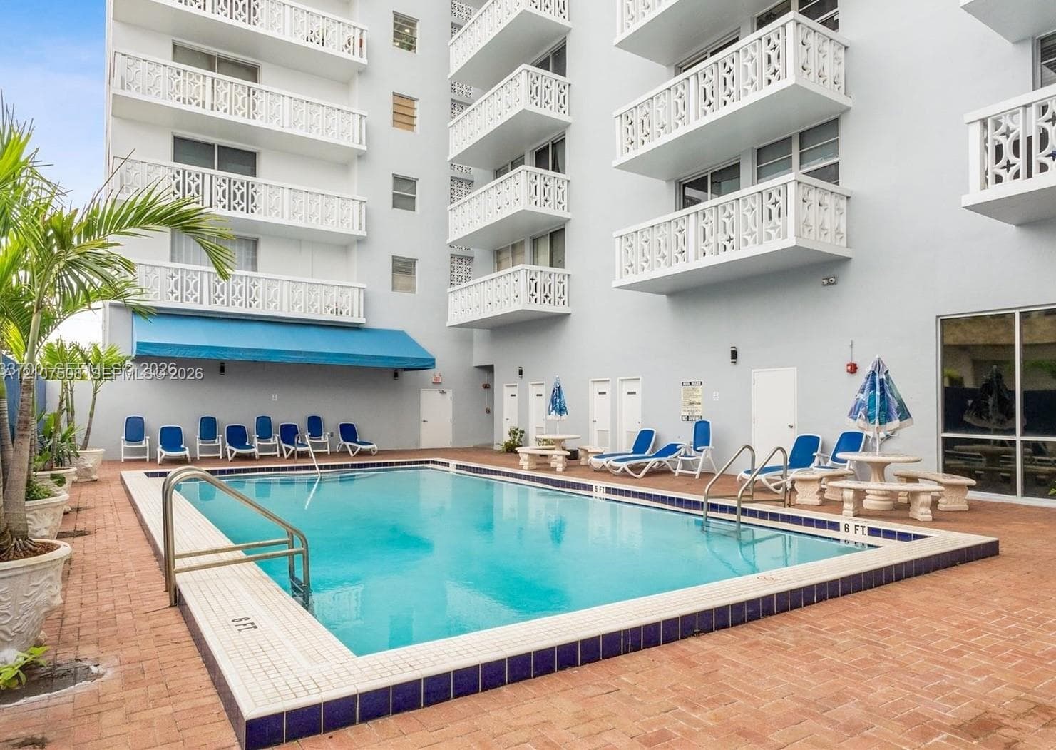 Swimming pool featuring a brick-paver deck, decorative metal balcony railings, and a blue retractable awning