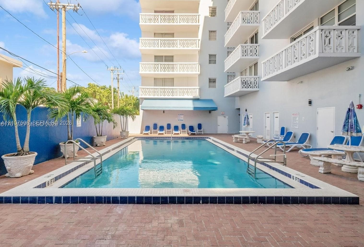 In-ground swimming pool with tile surround, red brick paver decking, and potted palm trees