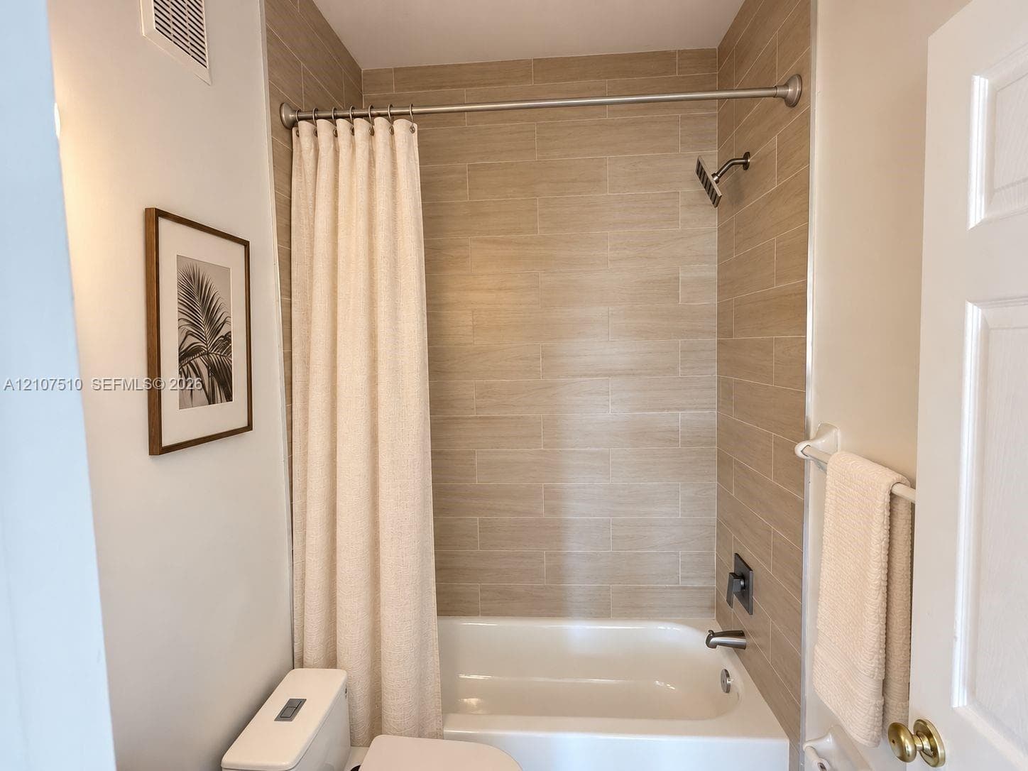 Full bathroom featuring horizontal wood-finish tile tub surround, stainless steel shower head, and built-in white porcelain tub