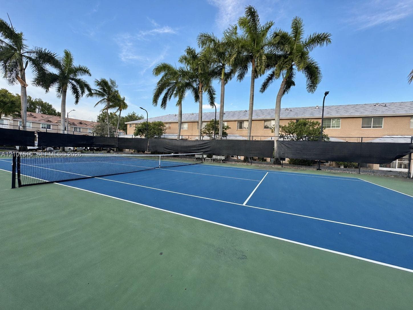 Tennis court featuring a hard surface, perimeter fencing, and established palm trees
