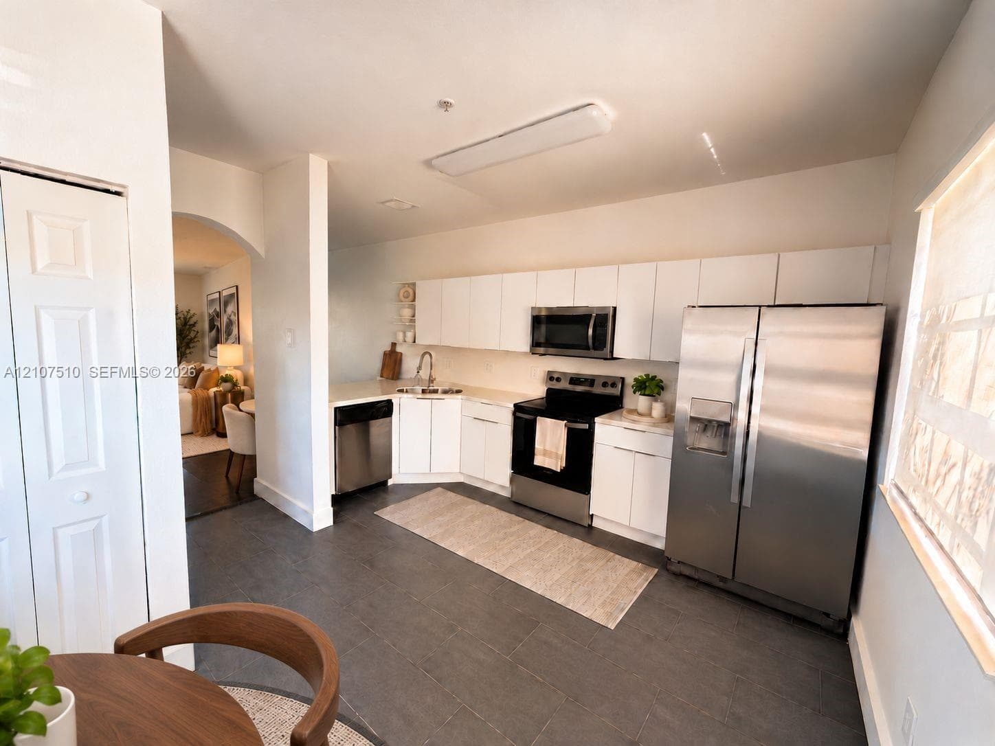 Kitchen featuring white flat-panel cabinetry, stainless steel appliances, solid-surface countertops, and dark tile flooring