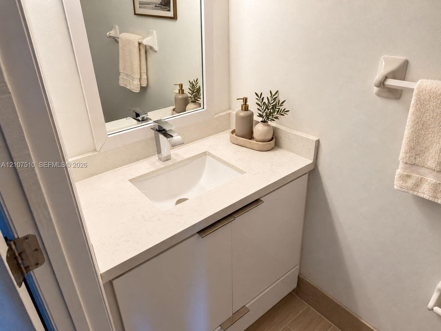 Glossy white vanity featuring a rectangular under-mount sink, light-toned stone countertop, polished chrome single-handle faucet, and hardware-mounted towel bars