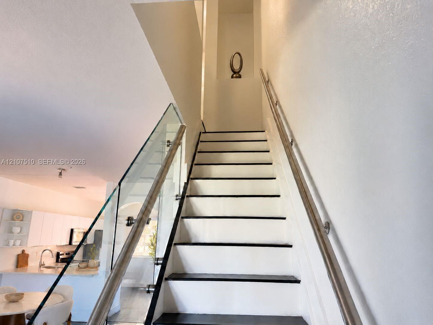 Staircase featuring glass panel railings, dark-finish treads, a mounted metal handrail, and a recessed wall niche