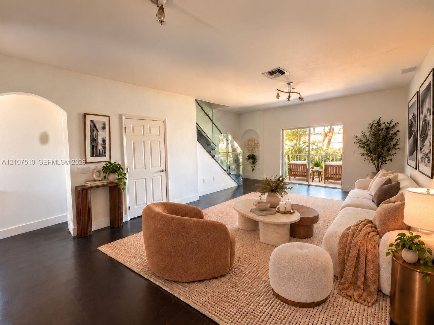 Open-concept interior featuring dark wood-finish flooring, an arched entryway, a glass-panel staircase railing, and sliding glass doors