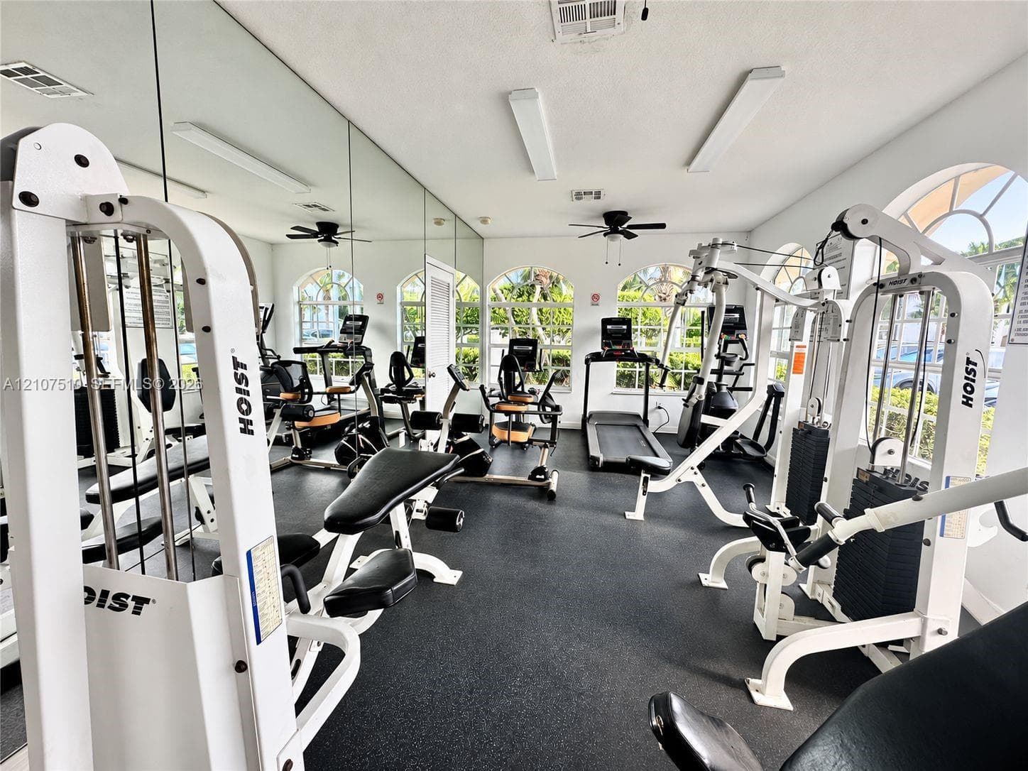 Fitness facility featuring rubberized flooring, floor-to-ceiling wall mirrors, arched windows, and integrated ceiling fans