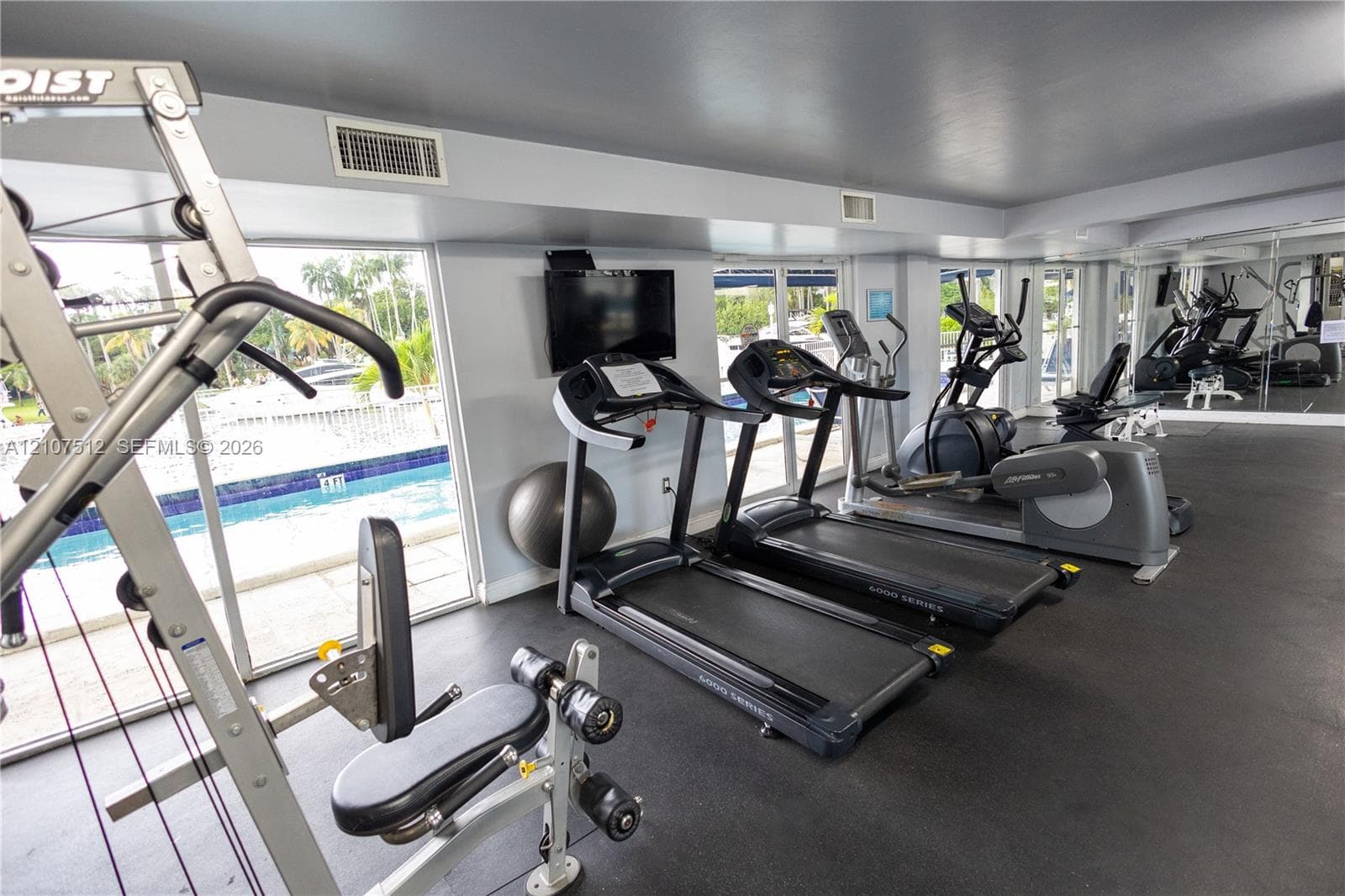 Fitness center featuring durable rubber flooring, floor-to-ceiling windows, wall-mounted television, and mirrored walls