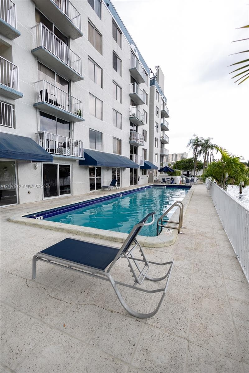 In-ground swimming pool with a stone-paver deck, blue canvas retractable awnings, and multi-level balconies