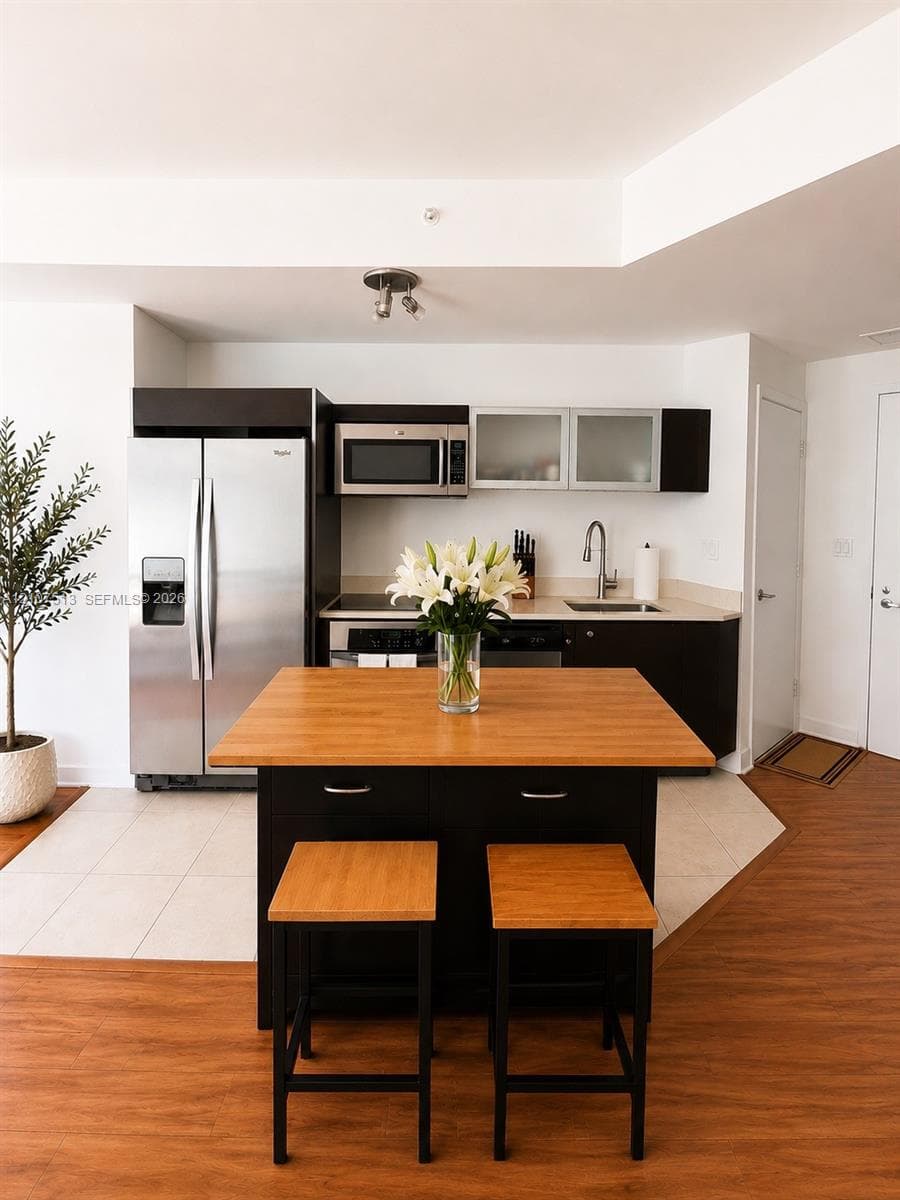 Kitchen featuring stainless steel appliances, dark cabinetry, frosted glass cabinet doors, wood-finish countertop on center island, and wood-finish flooring