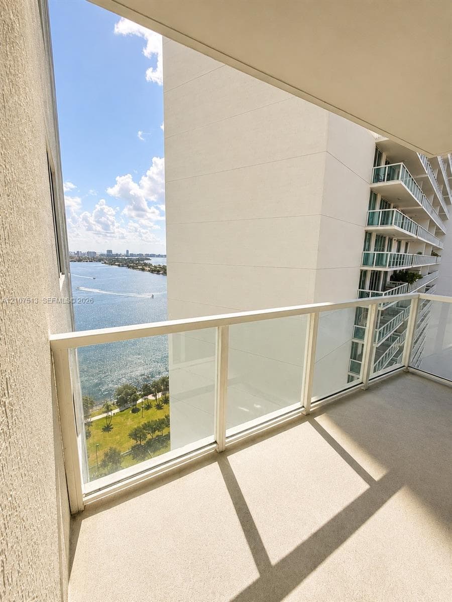 Private balcony featuring a glass-panel railing and concrete flooring, overlooking the water and shoreline