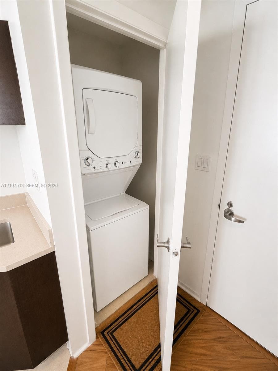 Stacked laundry center with white finish, integrated cabinetry with solid-surface countertop, and wood-finish flooring