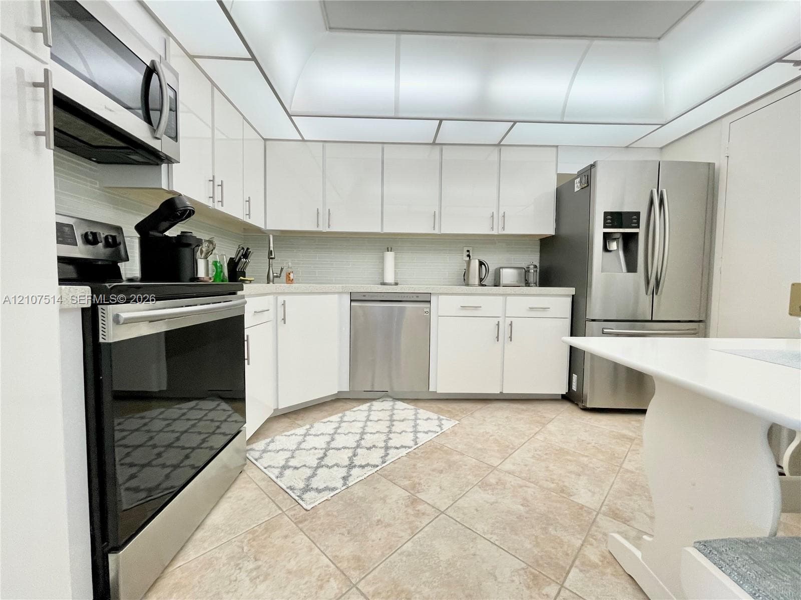 Kitchen featuring white cabinetry, stainless steel appliances, tile flooring, and integrated ceiling lighting