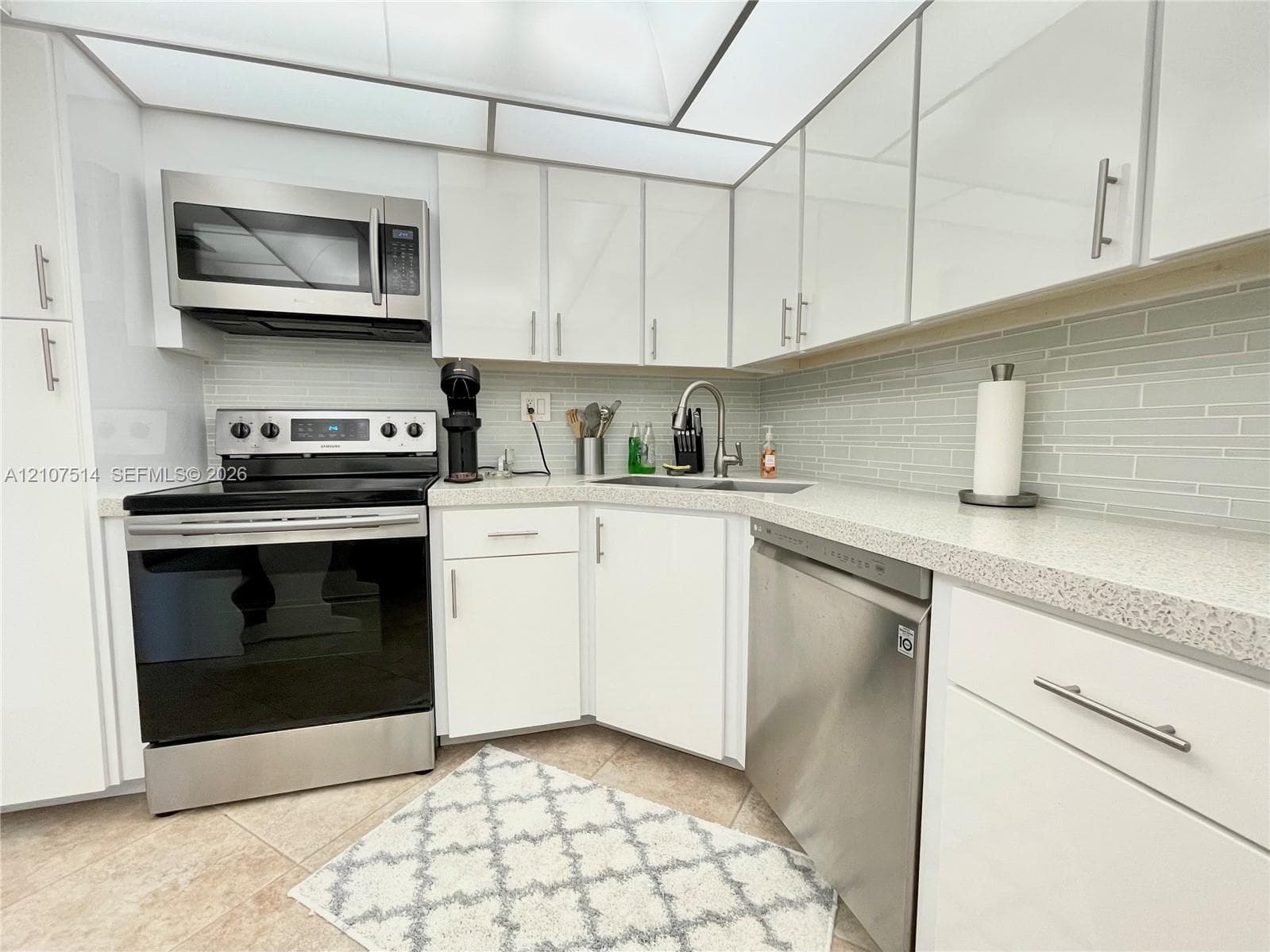 Kitchen featuring white cabinetry with metallic hardware, stone-composite countertops, stainless steel appliances, and a glass-tile backsplash