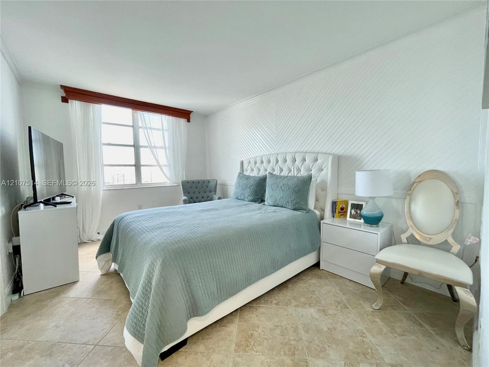 Bedroom featuring neutral tile flooring, herringbone-patterned wall paneling, and a large multi-pane window with a wood-finish valance
