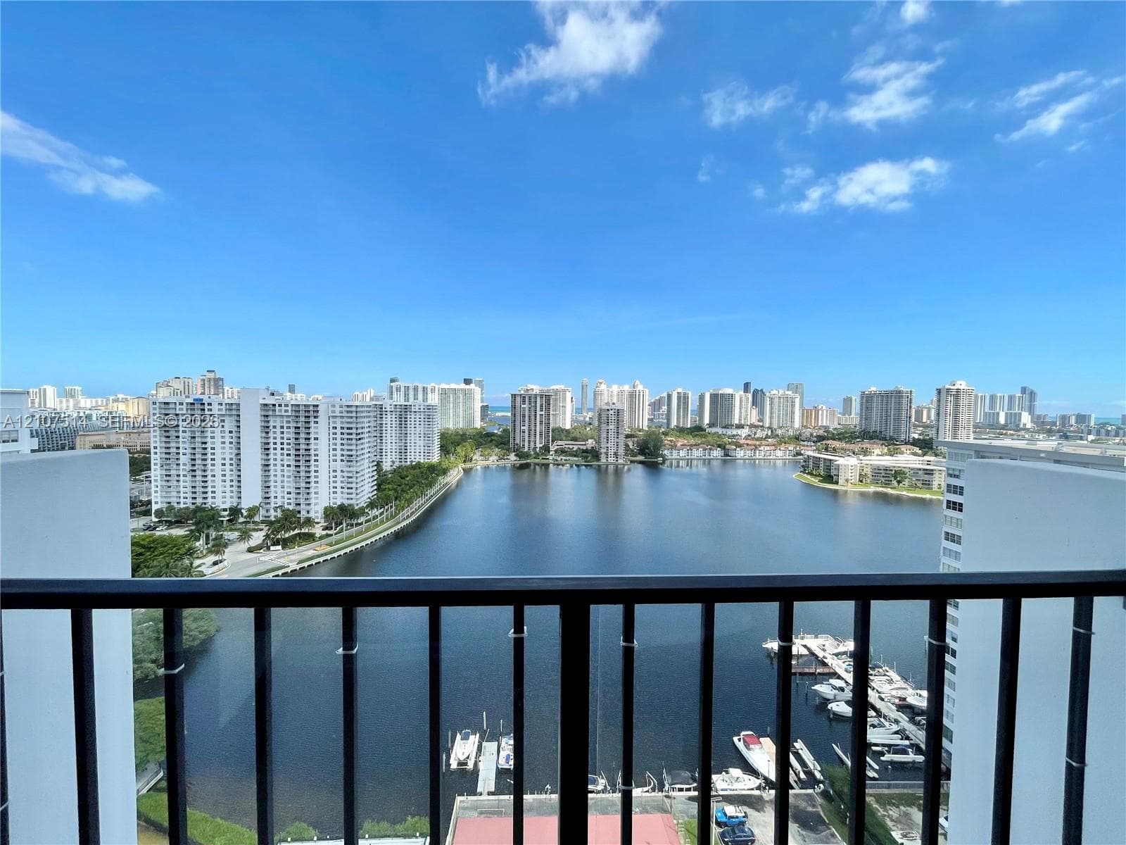Elevated balcony featuring a black metal railing, overlooking a large waterway, boat slips, and a cityscape skyline