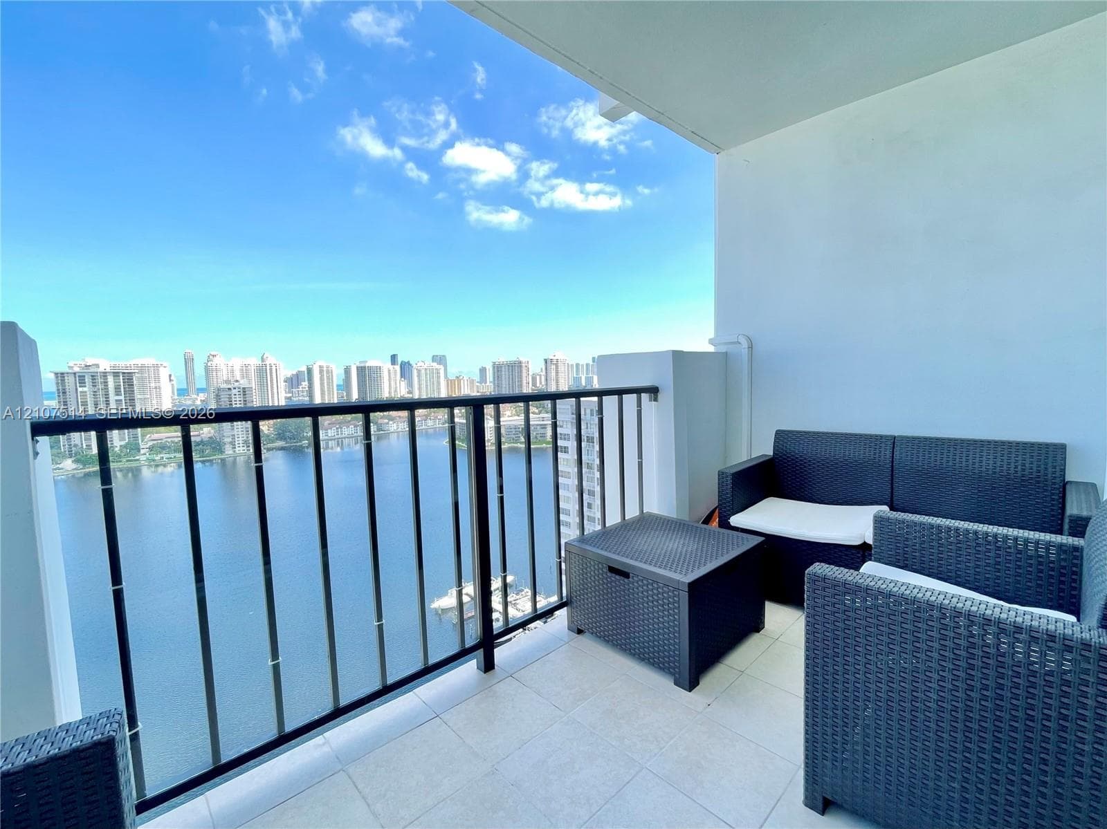 Covered balcony featuring tile flooring and a black metal railing overlooking the water and urban skyline