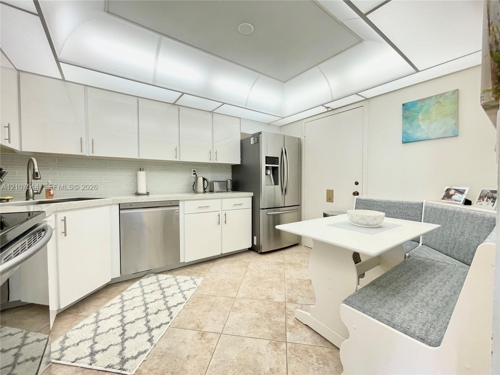 Kitchen featuring white cabinetry, stainless steel appliances, light-toned stone-finish countertops, tiled backsplash, and recessed cove lighting