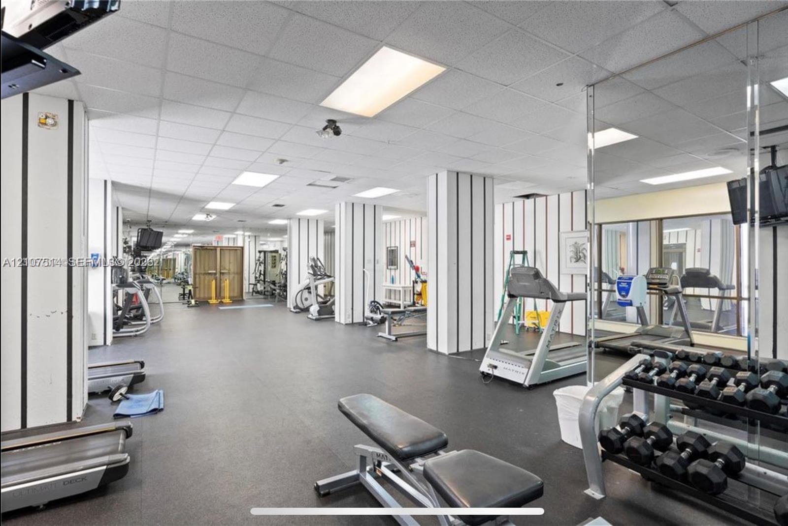 Fitness facility featuring rubberized flooring, mirrored walls, drop ceiling panels, and structural columns with vertical accent detailing