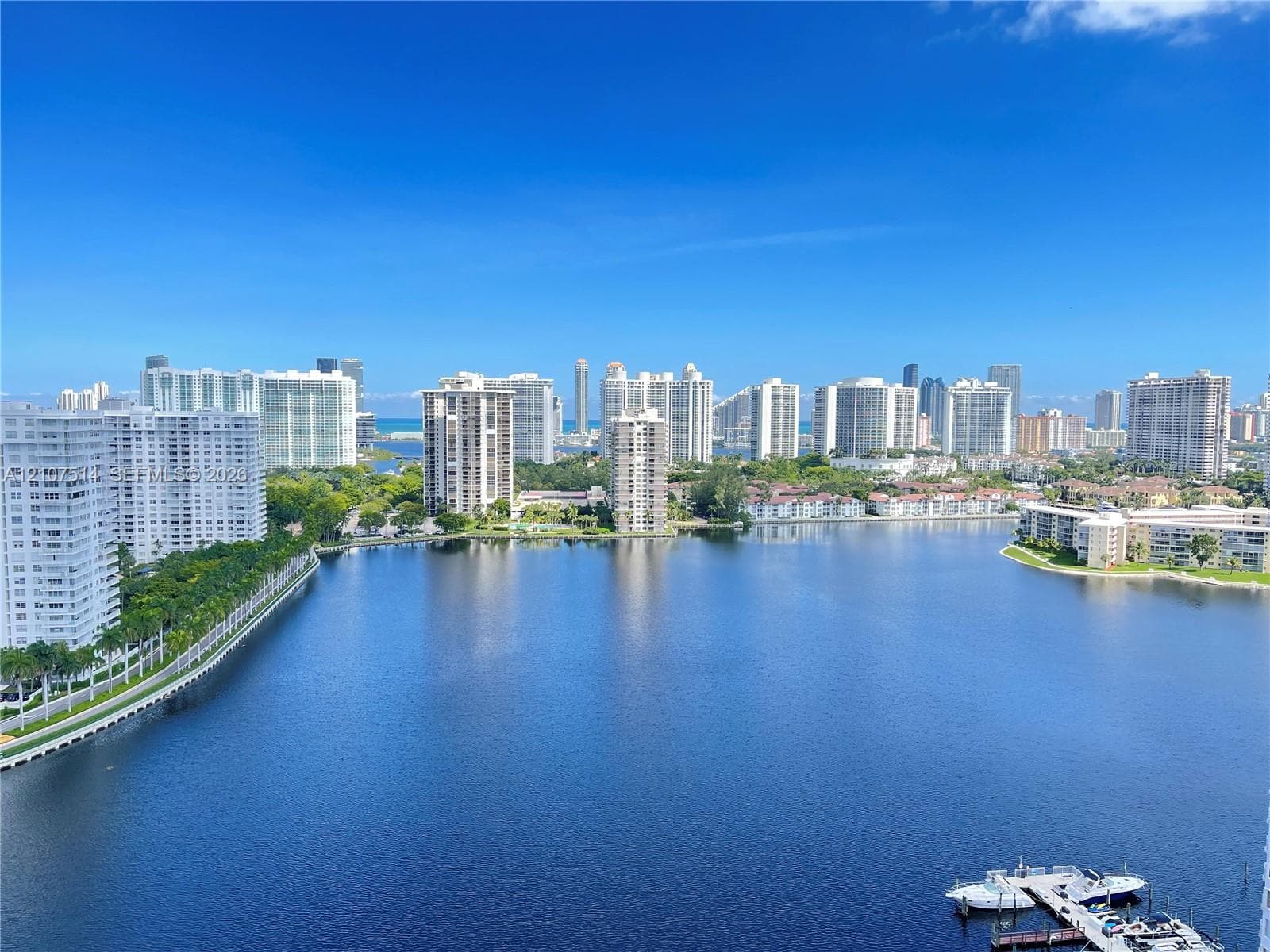 Expansive water frontage featuring a deep-water canal, boat docking structure, urban skyline backdrop, and dense perimeter landscaping